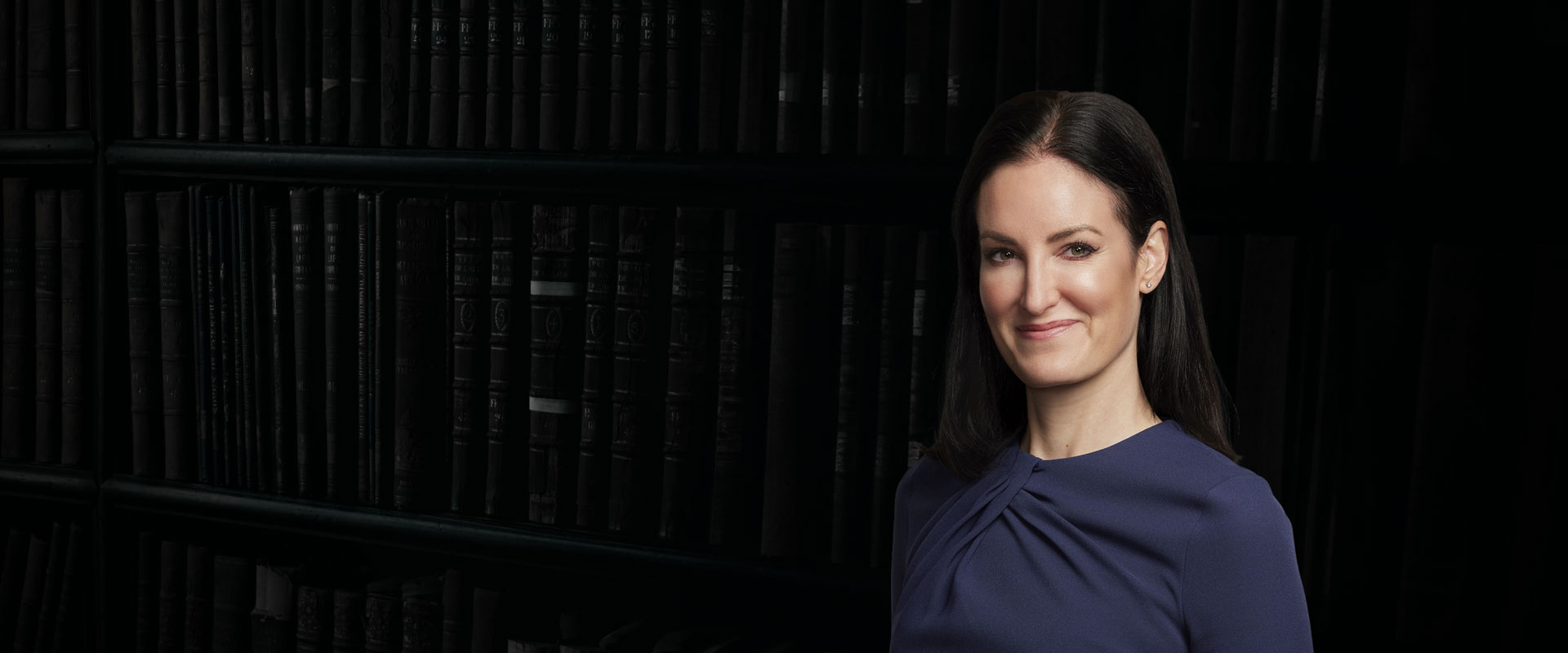 Maureen Hennessey, partner and trial lawyer at SHK Law, smiling in a navy dress with a decorative belt, professional portrait.