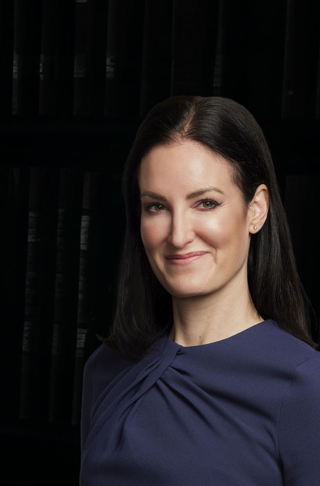 Maureen Hennessey, partner and trial lawyer at SHK Law, professional portrait in navy dress with decorative belt.”